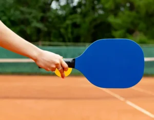 The hand of a pickleball player, racquet and ball, about to serve