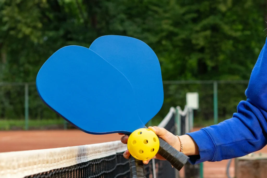 Two paddles and a ball in hand at the net